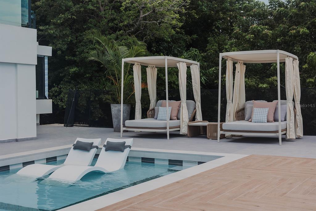 A swimming pool with two lounge chairs sits in front of two outdoor canopy beds — 13-14 PORT ROAD, HUMACAO, PR