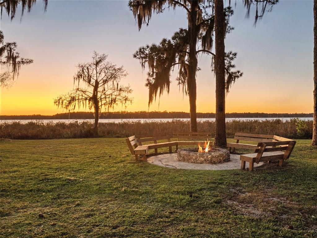 A stone fire pit with wooden benches sits on a grassy lawn at sunset — 14051 MARINE COURT, ORLANDO, FL