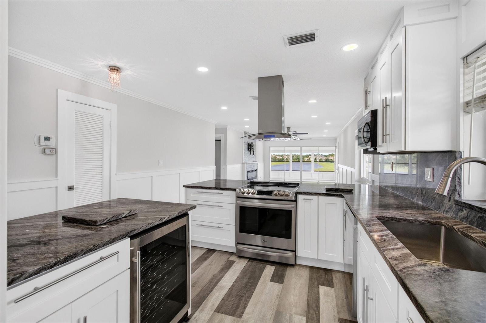 A modern kitchen features white cabinets, dark granite countertops, stainless steel appliances, and wood-look flooring — 5650 Spindle Palm Court # D, Delray Beach FL 33484, DELRAY BEACH, FL