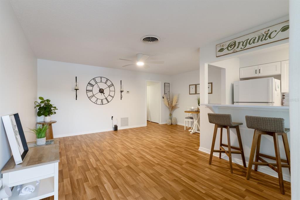 A living room with wood-look flooring, a large wall clock, and a kitchen breakfast bar — 4444 SWIFT ROAD UNIT 4, SARASOTA, FL