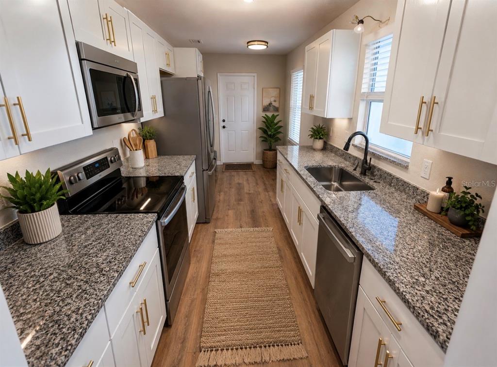 A galley kitchen features white cabinets, granite countertops, stainless steel appliances, and wood-look flooring — 8577 NE 157TH COURT, SILVER SPRINGS, FL
