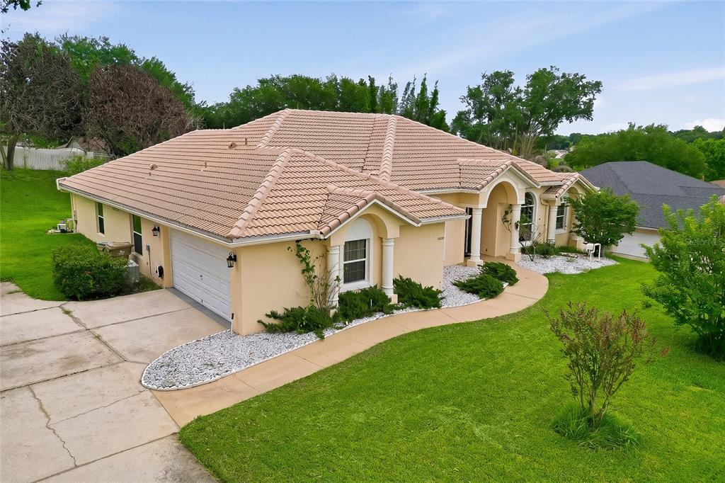 An elevated exterior view of a single-story beige house with a tiled roof and driveway — 10708 BELO HORIZONTE AVENUE, CLERMONT, FL