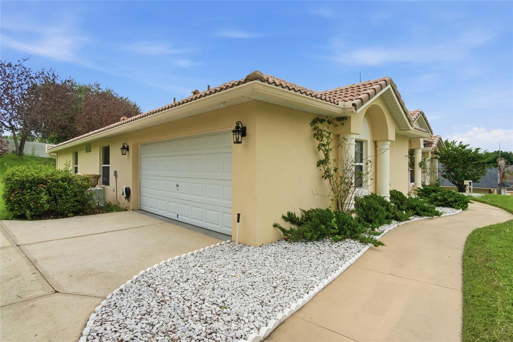 A beige stucco house with a white garage door, tile roof, and landscaped front yard — 10708 BELO HORIZONTE AVENUE, CLERMONT, FL