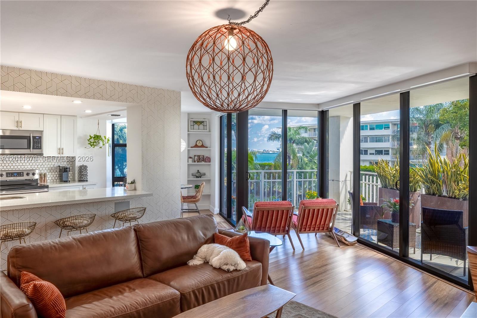 A living room with a brown leather sofa, spherical pendant light, and sliding glass balcony doors — 4000 Towerside Ter # 308, Miami FL 33138, MIAMI, FL
