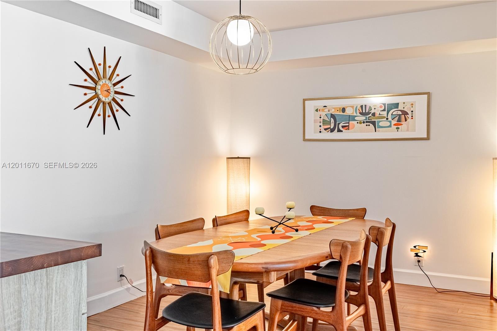 A dining room features a wooden table, mid-century modern chairs, and a starburst wall clock — 4000 Towerside Ter # 308, Miami FL 33138, MIAMI, FL