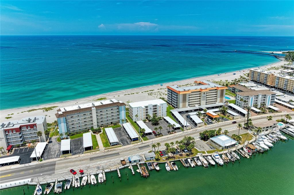 An aerial view shows beachfront condominiums, a parking lot, and a boat dock — 1100 TARPON CENTER DRIVE UNIT 104, VENICE, FL