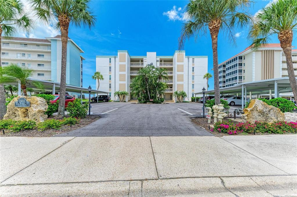 An exterior view of a multi-story apartment building with a parking lot and palm trees — 1100 TARPON CENTER DRIVE UNIT 104, VENICE, FL