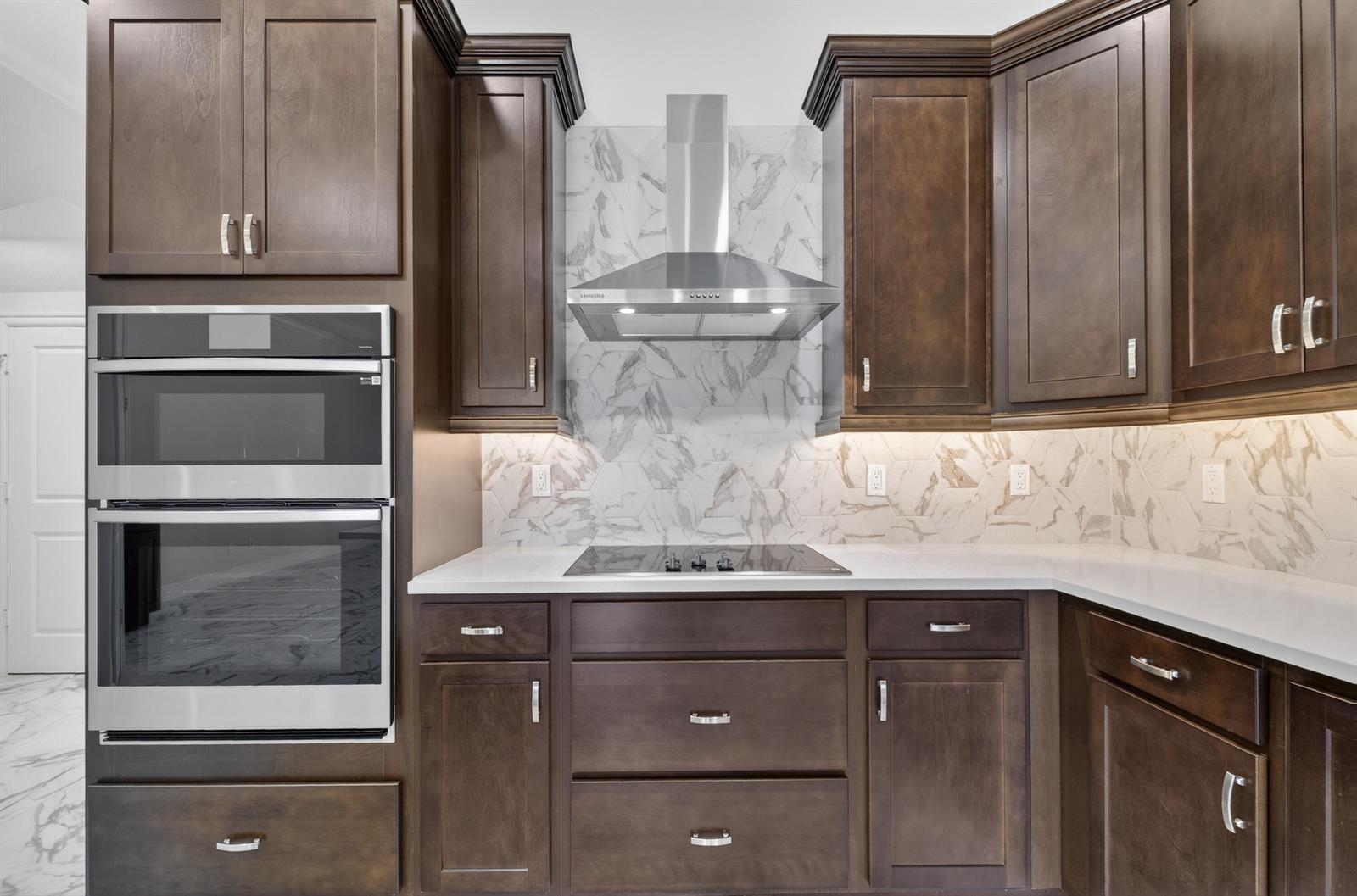 A kitchen features dark wood cabinets, stainless steel appliances, and a marble-patterned tile backsplash — 1805 Bridgepointe Circle # 1, Vero Beach FL 32967, VERO BEACH, FL