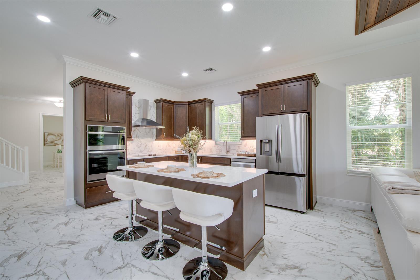 A kitchen features dark wood cabinets, a white marble island, and stainless steel appliances — 1805 Bridgepointe Circle # 1, Vero Beach FL 32967, VERO BEACH, FL