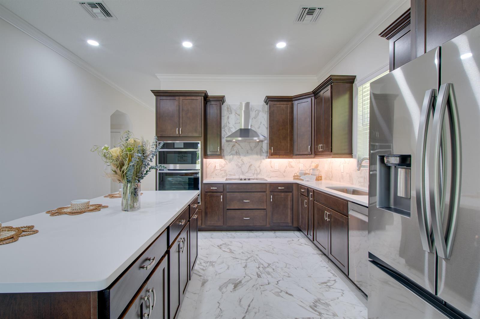 A kitchen features dark wood cabinets, white marble countertops, stainless steel appliances, and marble flooring — 1805 Bridgepointe Circle # 1, Vero Beach FL 32967, VERO BEACH, FL