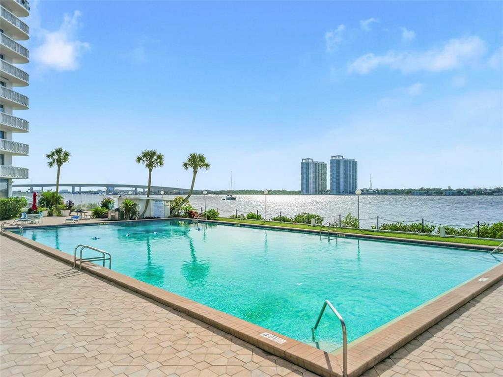 A rectangular swimming pool sits on a paved deck overlooking a bay with a bridge — 925 N HALIFAX AVENUE UNIT 103, DAYTONA BEACH, FL