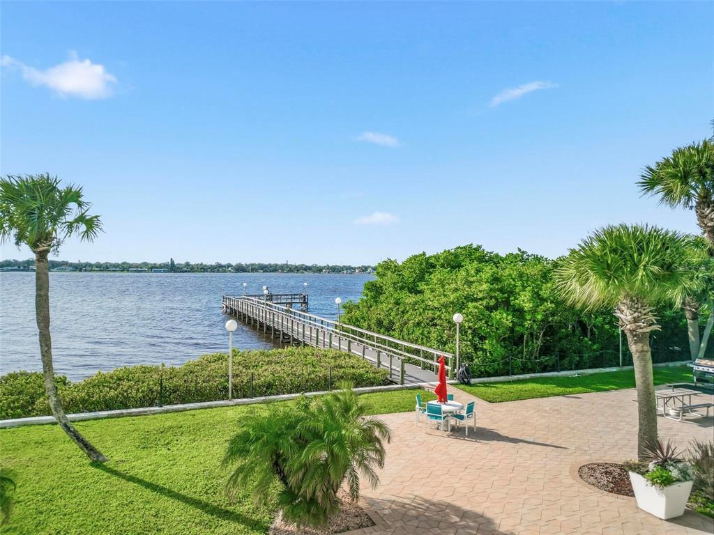 A paved patio with a table and chairs overlooks a long wooden pier and water — 925 N HALIFAX AVENUE UNIT 103, DAYTONA BEACH, FL