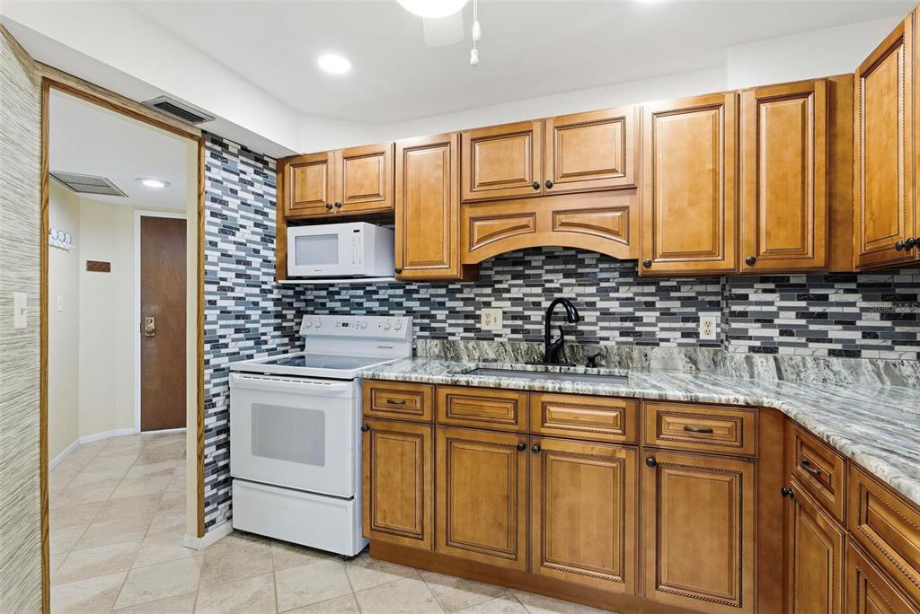A kitchen features wood cabinets, a white stove, a patterned backsplash, and granite countertops — 925 N HALIFAX AVENUE UNIT 103, DAYTONA BEACH, FL