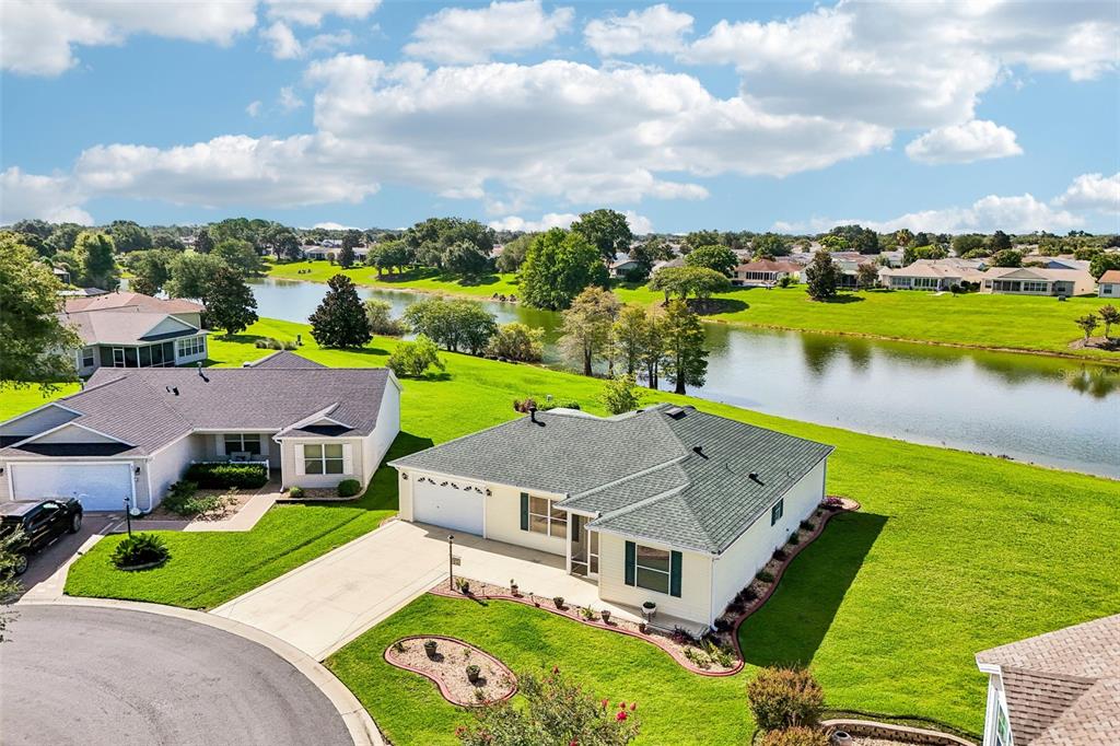 An aerial view shows two suburban houses with green lawns beside a large pond — 917 EASTMONT COURT, THE VILLAGES, FL