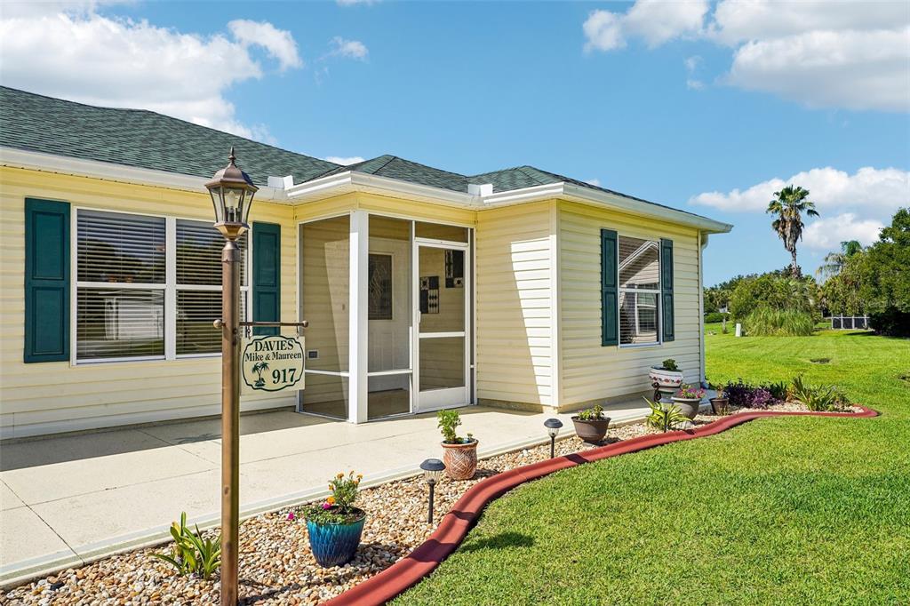 A yellow house with green shutters features a screened-in porch and a landscaped yard — 917 EASTMONT COURT, THE VILLAGES, FL