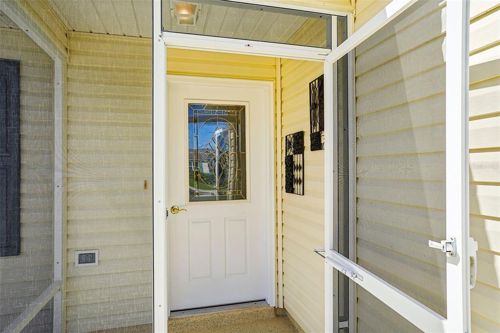 A white front door with a decorative glass insert sits inside a screened-in porch — 917 EASTMONT COURT, THE VILLAGES, FL