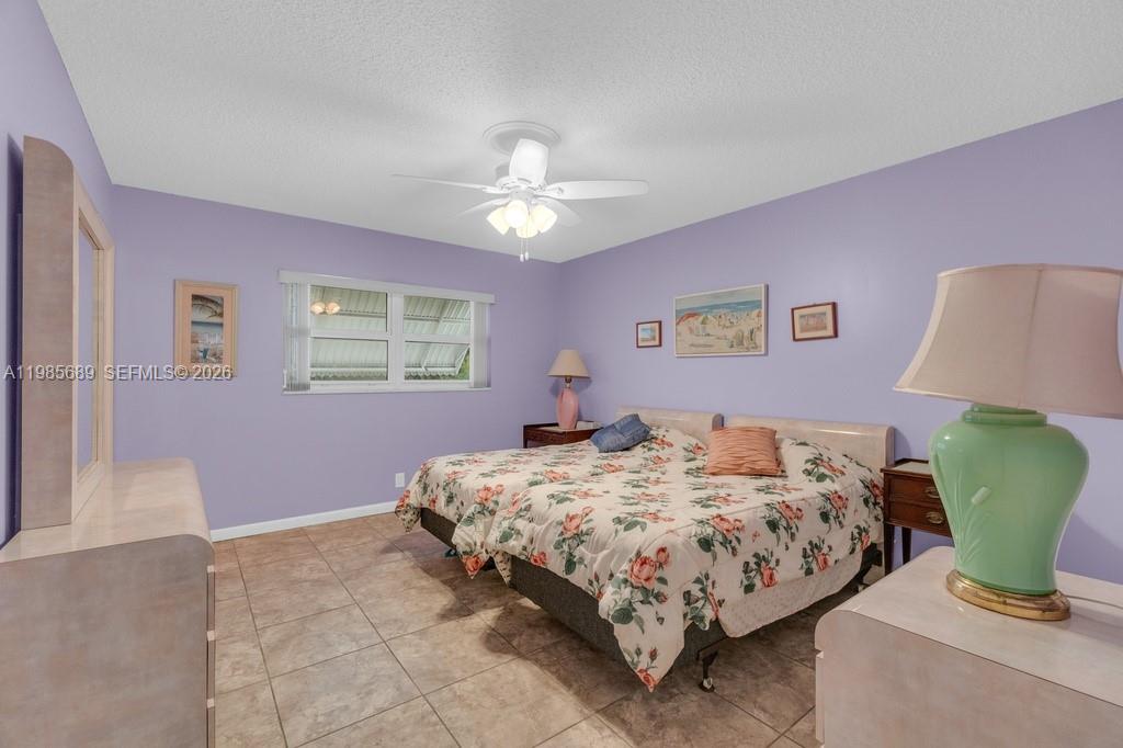 A bedroom features lavender walls, tile flooring, a floral bedspread, and a ceiling fan — 5300 Washington St # J218, Hollywood FL 33021, HOLLYWOOD, FL