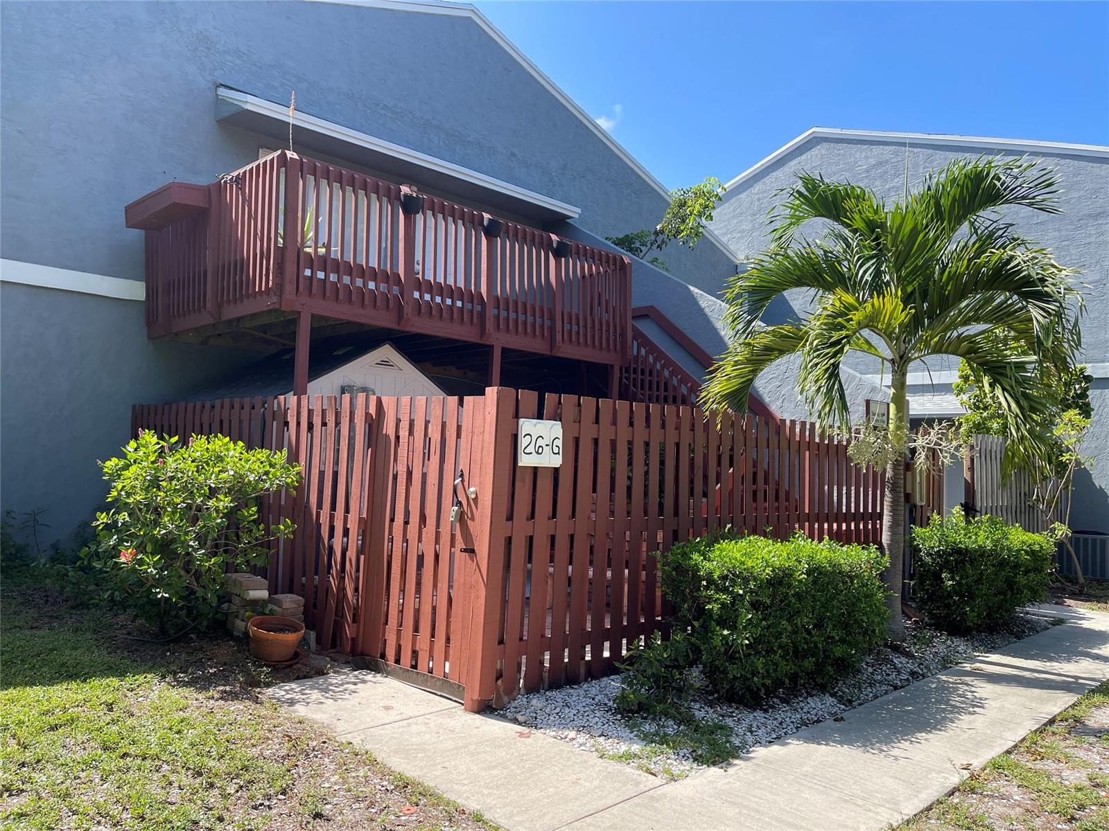 A two-story blue building features a wooden balcony and a fenced-in patio area — 26 Crossings Circle # G, Boynton Beach FL 33435, BOYNTON BEACH, FL