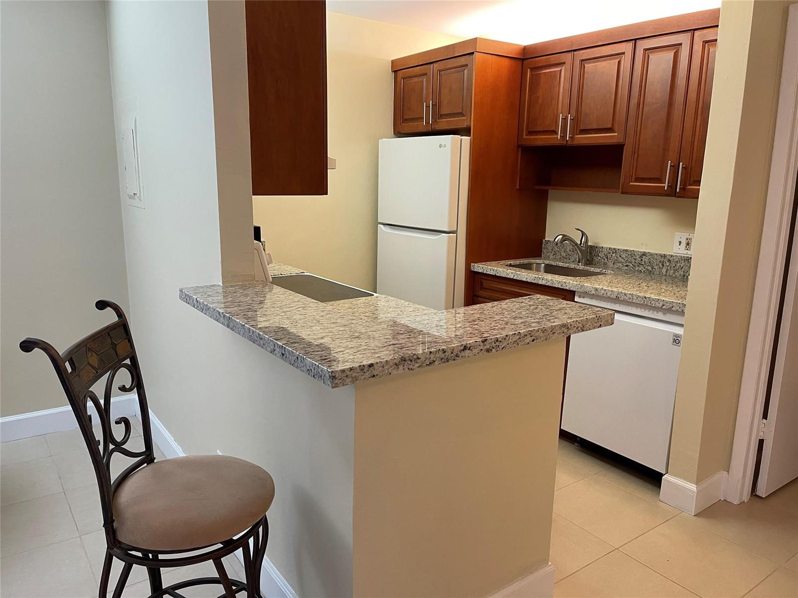 A kitchen with wood cabinets, granite countertops, white appliances, and a breakfast bar with seating — 26 Crossings Circle # G, Boynton Beach FL 33435, BOYNTON BEACH, FL