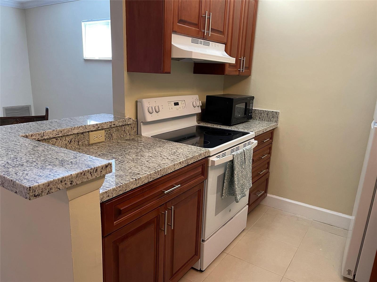 A kitchen features wood cabinets, granite countertops, a white stove, and a microwave — 26 Crossings Circle # G, Boynton Beach FL 33435, BOYNTON BEACH, FL