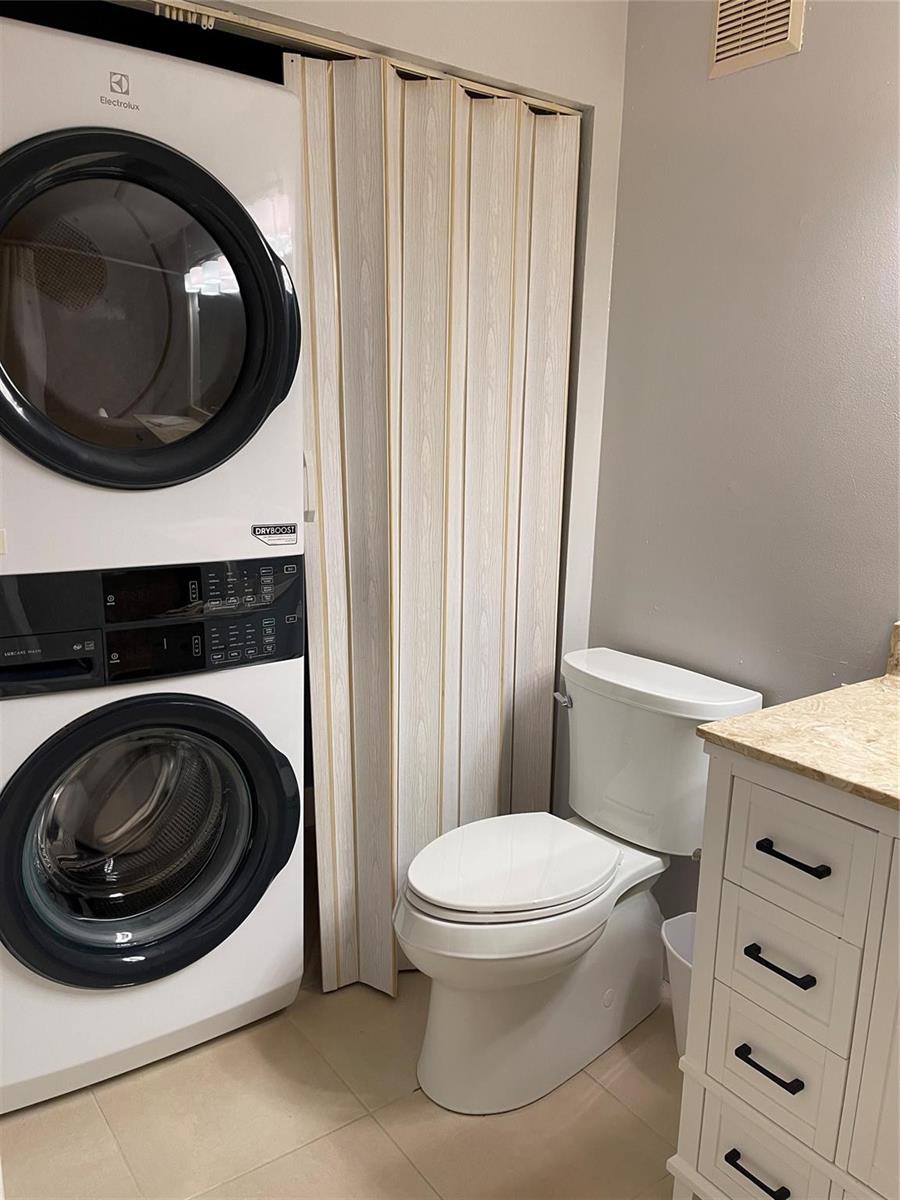 A laundry closet with a stacked washer and dryer sits next to a white toilet — 26 Crossings Circle # G, Boynton Beach FL 33435, BOYNTON BEACH, FL