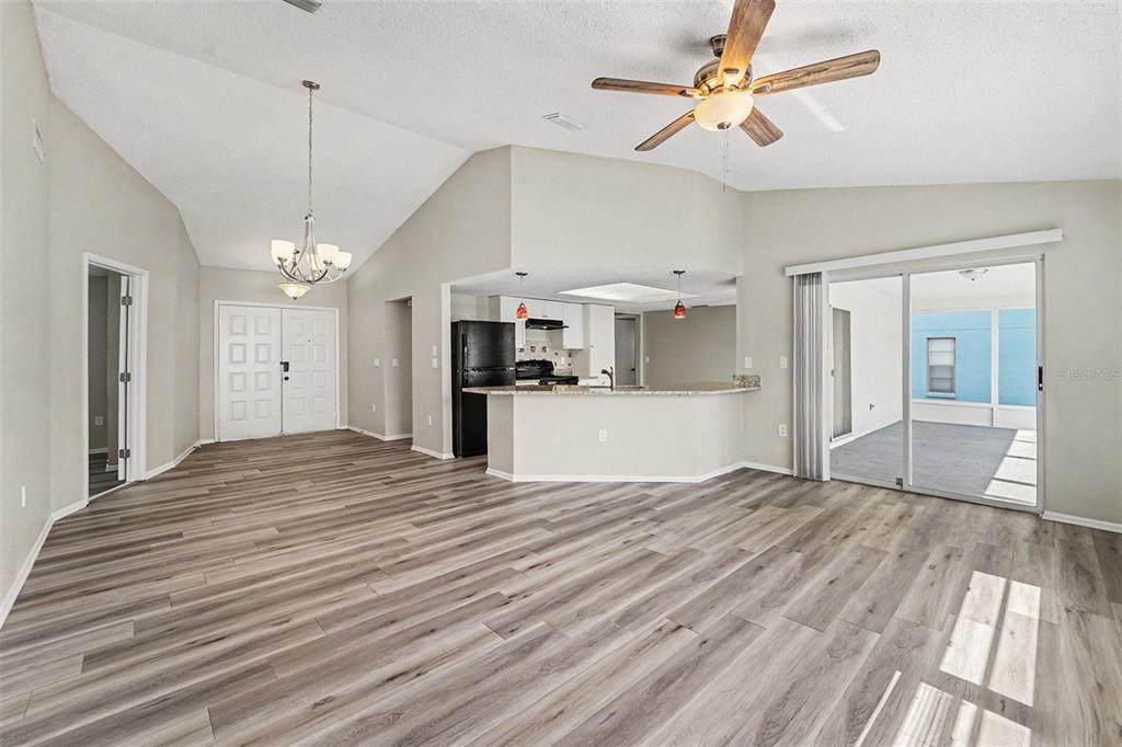 An open-concept living area features light wood-look flooring, vaulted ceilings, and a kitchen breakfast bar — 7336 ASHMORE DRIVE, NEW PORT RICHEY, FL