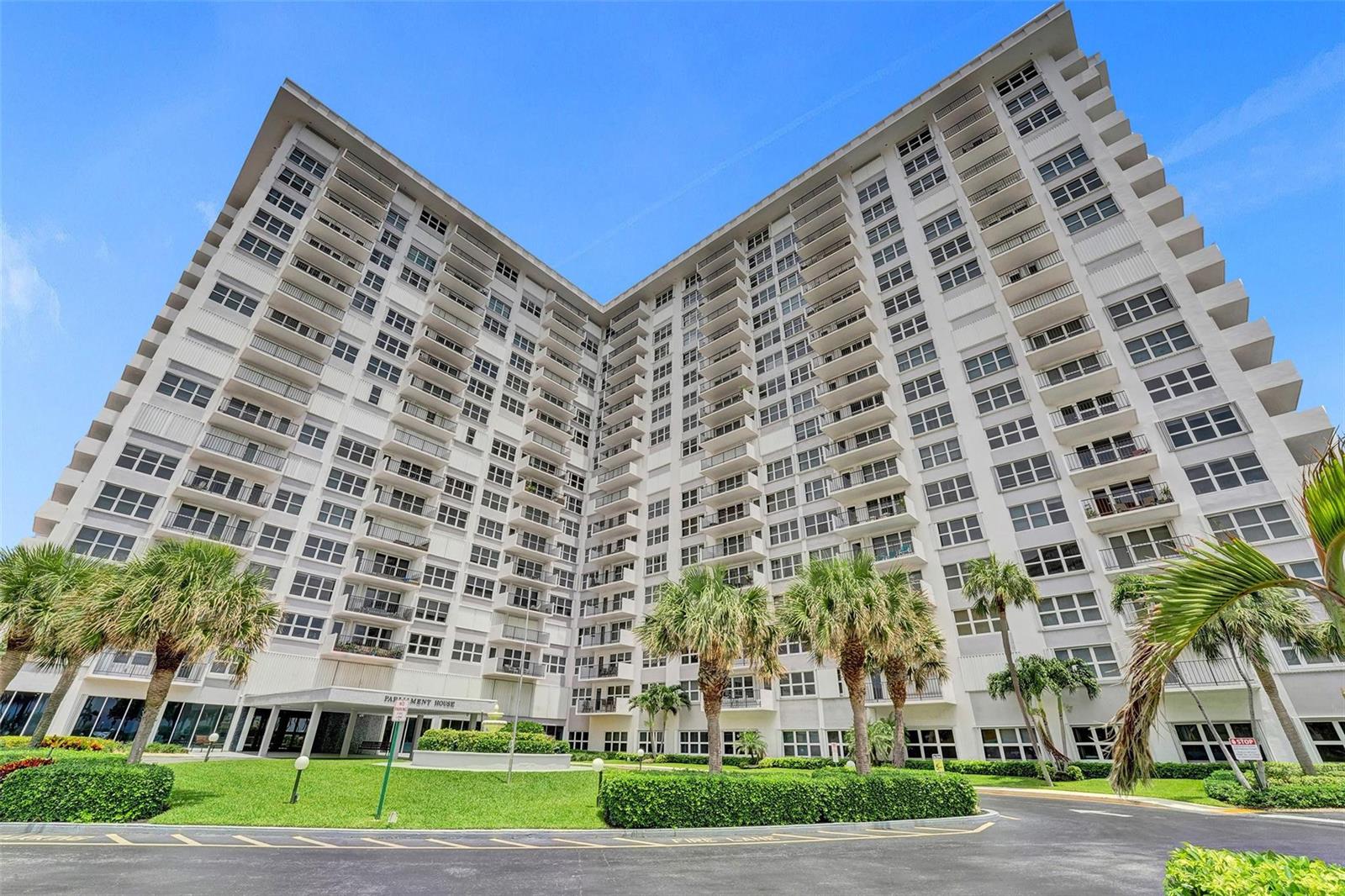 A low-angle exterior view of a large white apartment building with balconies and palm trees — 405 N Ocean Boulevard # 623, Pompano Beach FL 33062, POMPANO BEACH, FL
