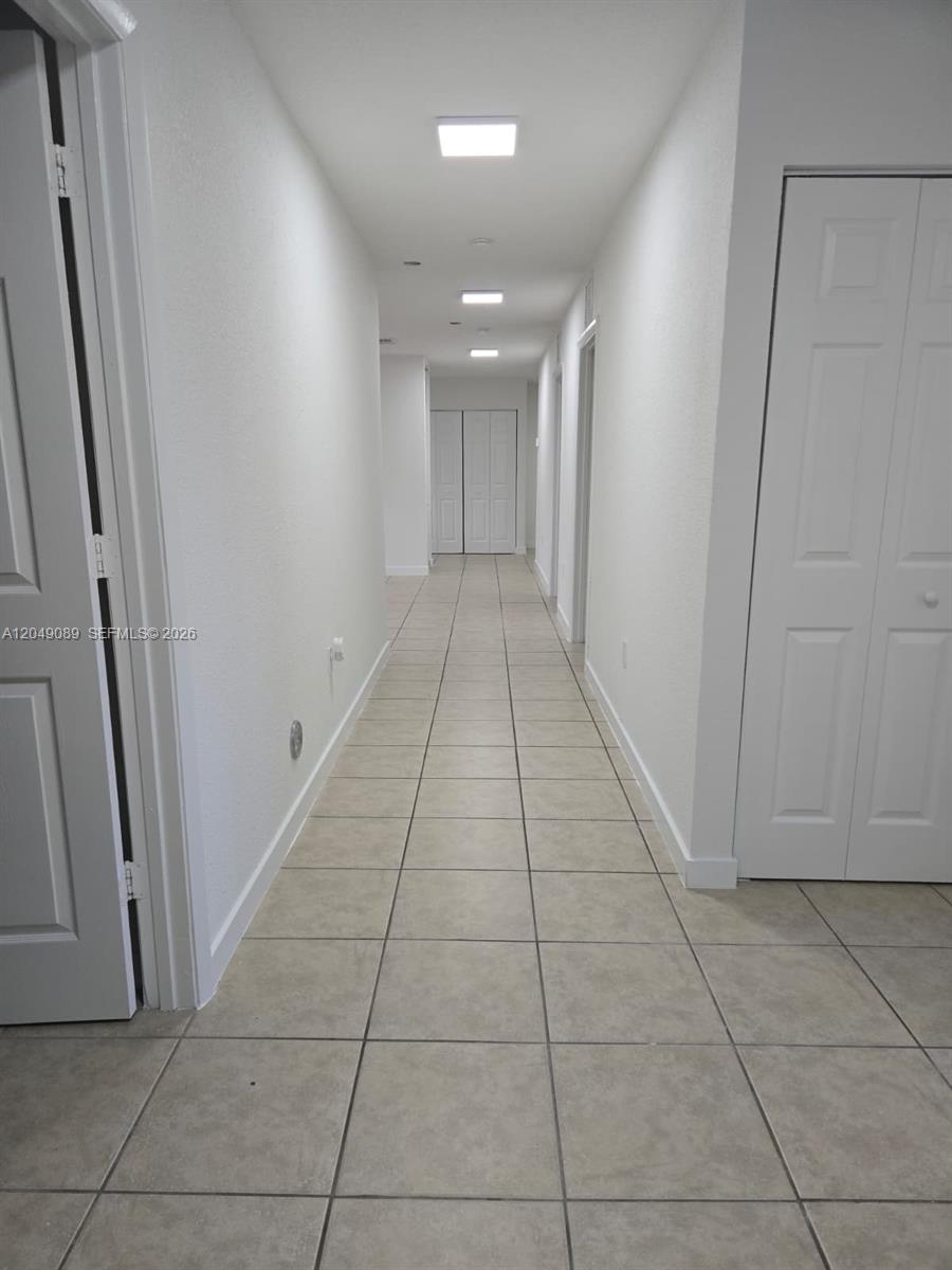 A long, narrow hallway features white walls, recessed ceiling lights, and light-colored tile flooring — MIAMI, FL