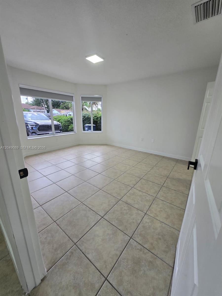 An empty room features beige tile flooring, white walls, and a large bay window — MIAMI, FL