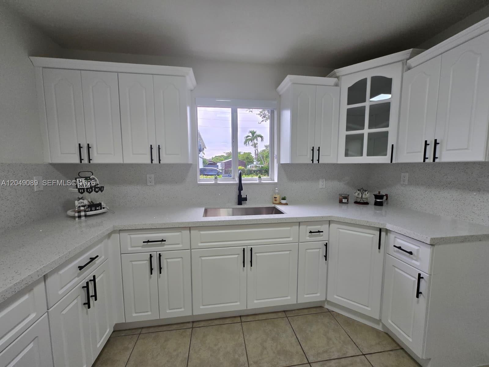 A kitchen features white cabinets, quartz countertops, a stainless steel sink, and tile flooring — MIAMI, FL