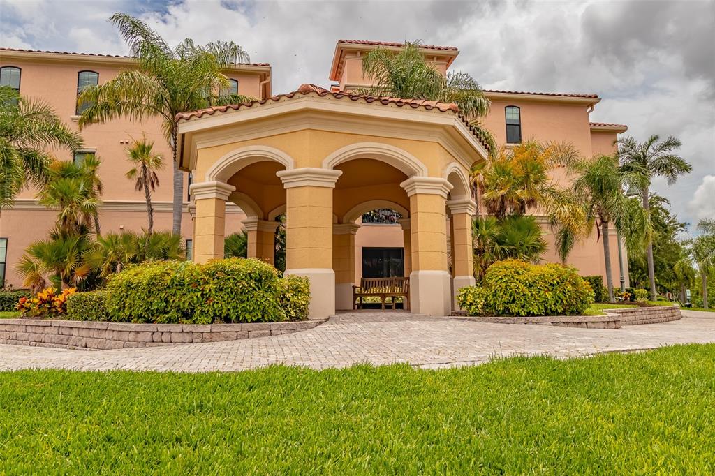 A beige building features a covered stone entryway with arched openings and surrounding palm trees — 2755 VIA CAPRI UNIT 1225, CLEARWATER, FL