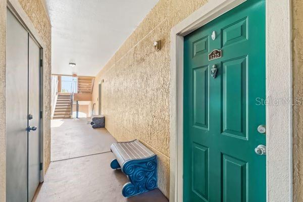 A teal front door with a number plate sits beside a bench in an outdoor hallway — 2755 VIA CAPRI UNIT 1225, CLEARWATER, FL