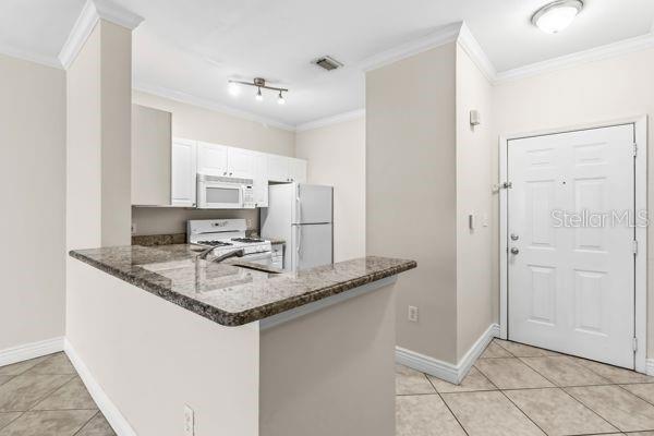 A kitchen with granite countertops, white cabinets, and stainless steel appliances opens to an entryway — 2755 VIA CAPRI UNIT 1225, CLEARWATER, FL