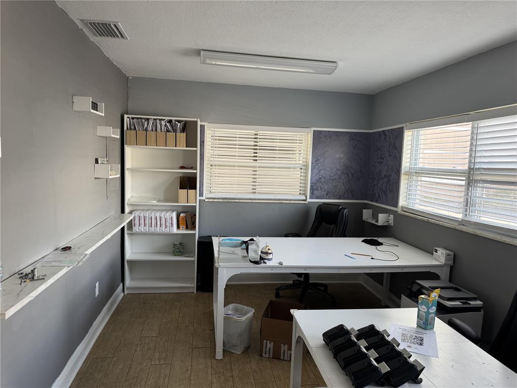 A home office features gray walls, white furniture, a bookshelf, and two windows with blinds — 1240 ROGERS STREET, CLEARWATER, FL