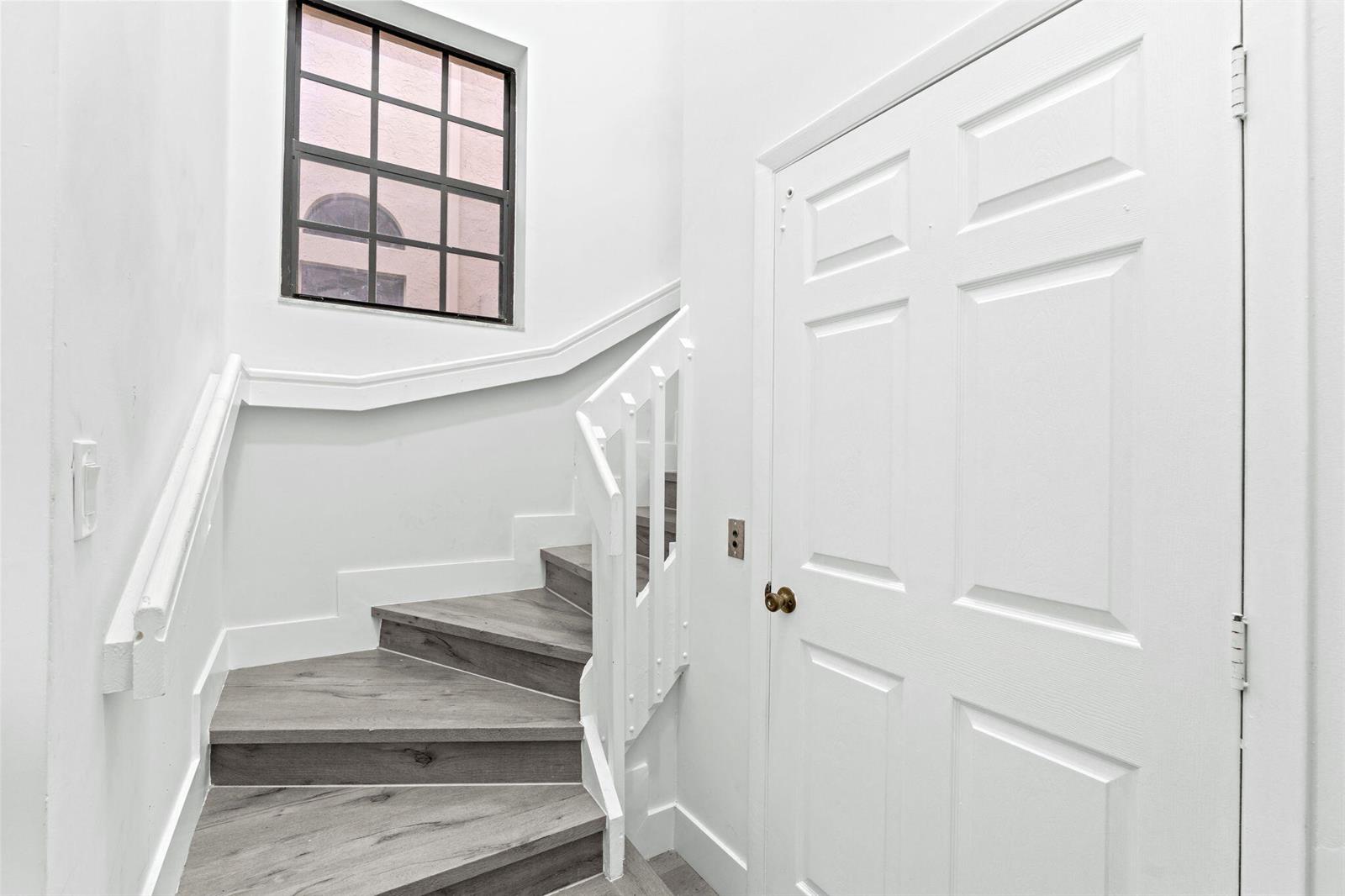 A staircase with wood-look flooring and white railings sits next to a white door — 5131 Europa Drive # I, Boynton Beach FL 33437, BOYNTON BEACH, FL