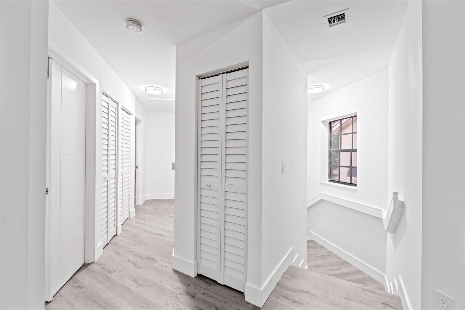 A bright hallway with white walls, light wood-look flooring, and several louvered closet doors — 5131 Europa Drive # I, Boynton Beach FL 33437, BOYNTON BEACH, FL