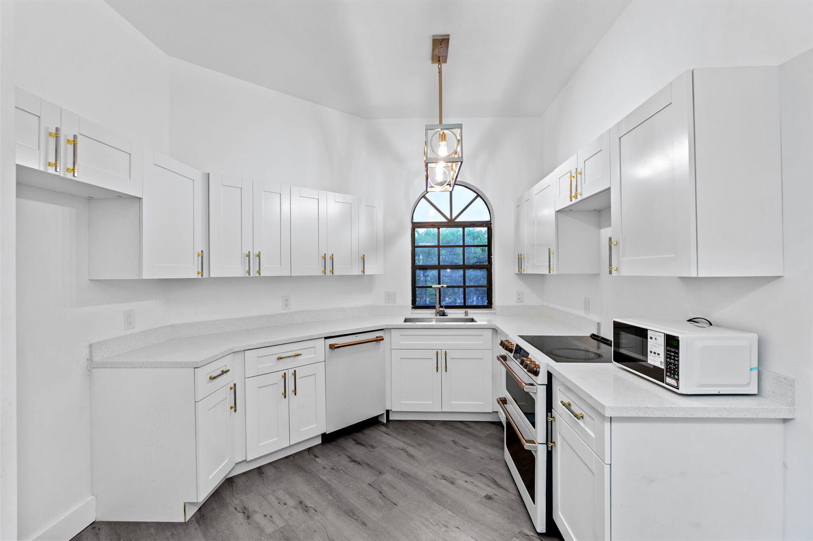 A white kitchen features shaker cabinets, quartz countertops, stainless steel appliances, and gray wood flooring — 5131 Europa Drive # I, Boynton Beach FL 33437, BOYNTON BEACH, FL