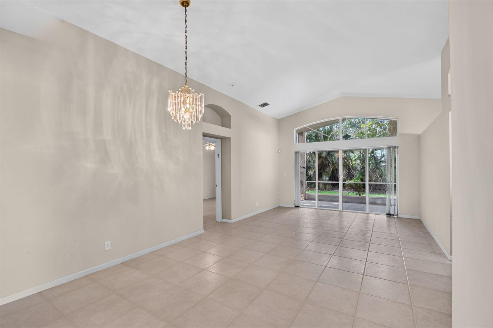 An empty living room with beige tile floors, a crystal chandelier, and large sliding glass doors — 9840 Arbor View Drive S, Boynton Beach FL 33437, BOYNTON BEACH, FL