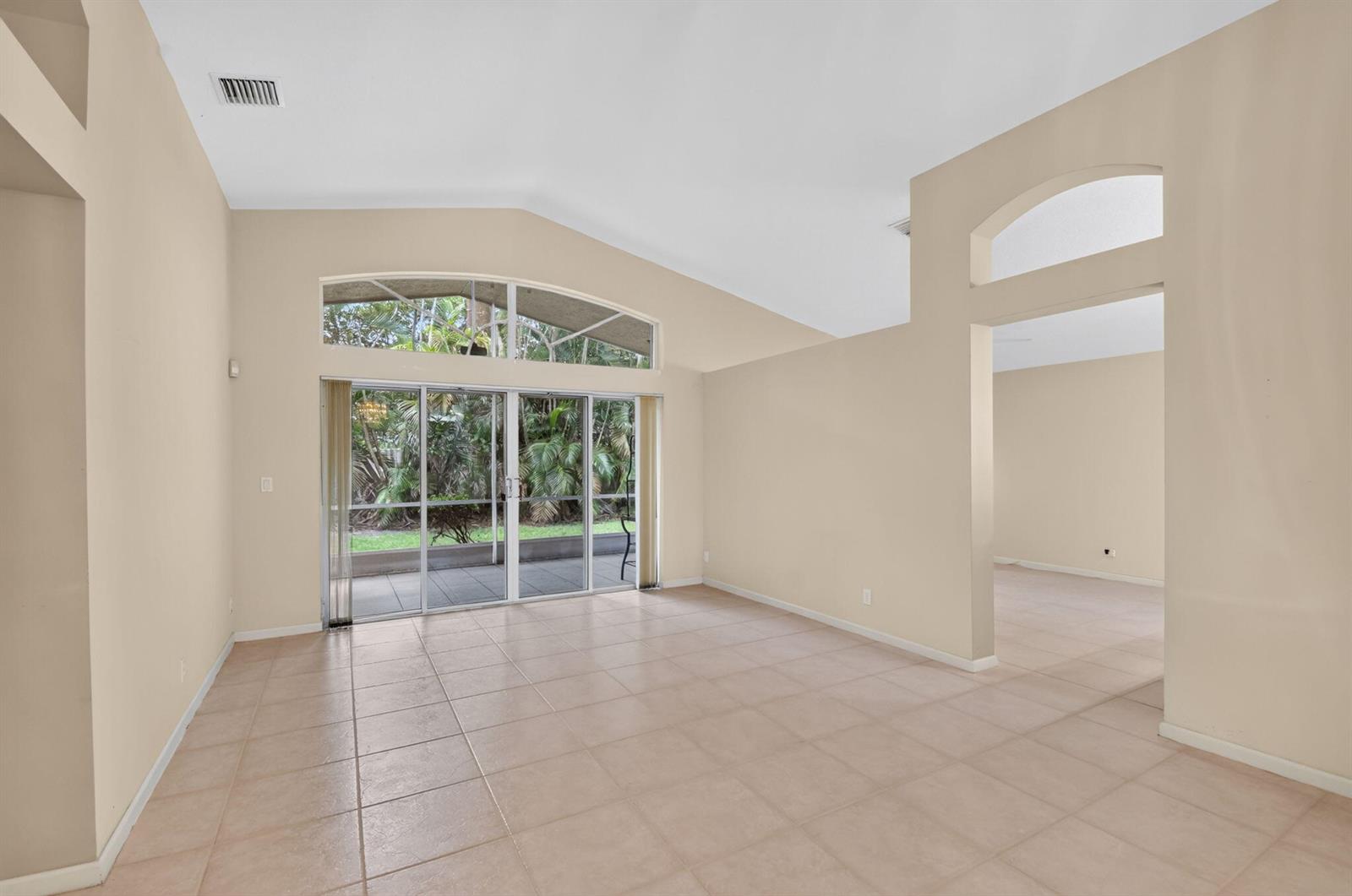 An empty living room with beige tile floors, vaulted ceilings, and sliding glass patio doors — 9840 Arbor View Drive S, Boynton Beach FL 33437, BOYNTON BEACH, FL
