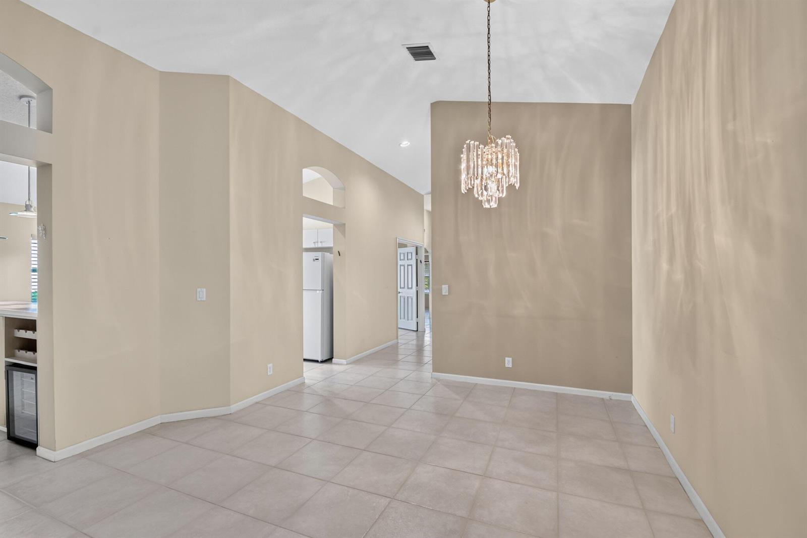 A dining area features tile flooring, beige walls, a crystal chandelier, and vaulted ceilings — 9840 Arbor View Drive S, Boynton Beach FL 33437, BOYNTON BEACH, FL