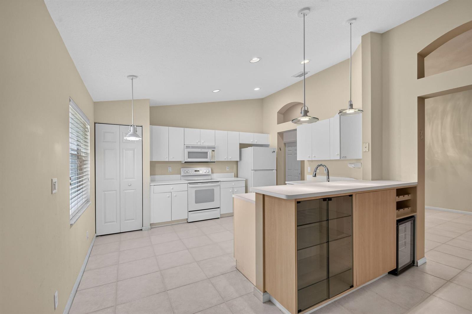A kitchen features white cabinets, white appliances, a light-colored island, and beige tile flooring — 9840 Arbor View Drive S, Boynton Beach FL 33437, BOYNTON BEACH, FL