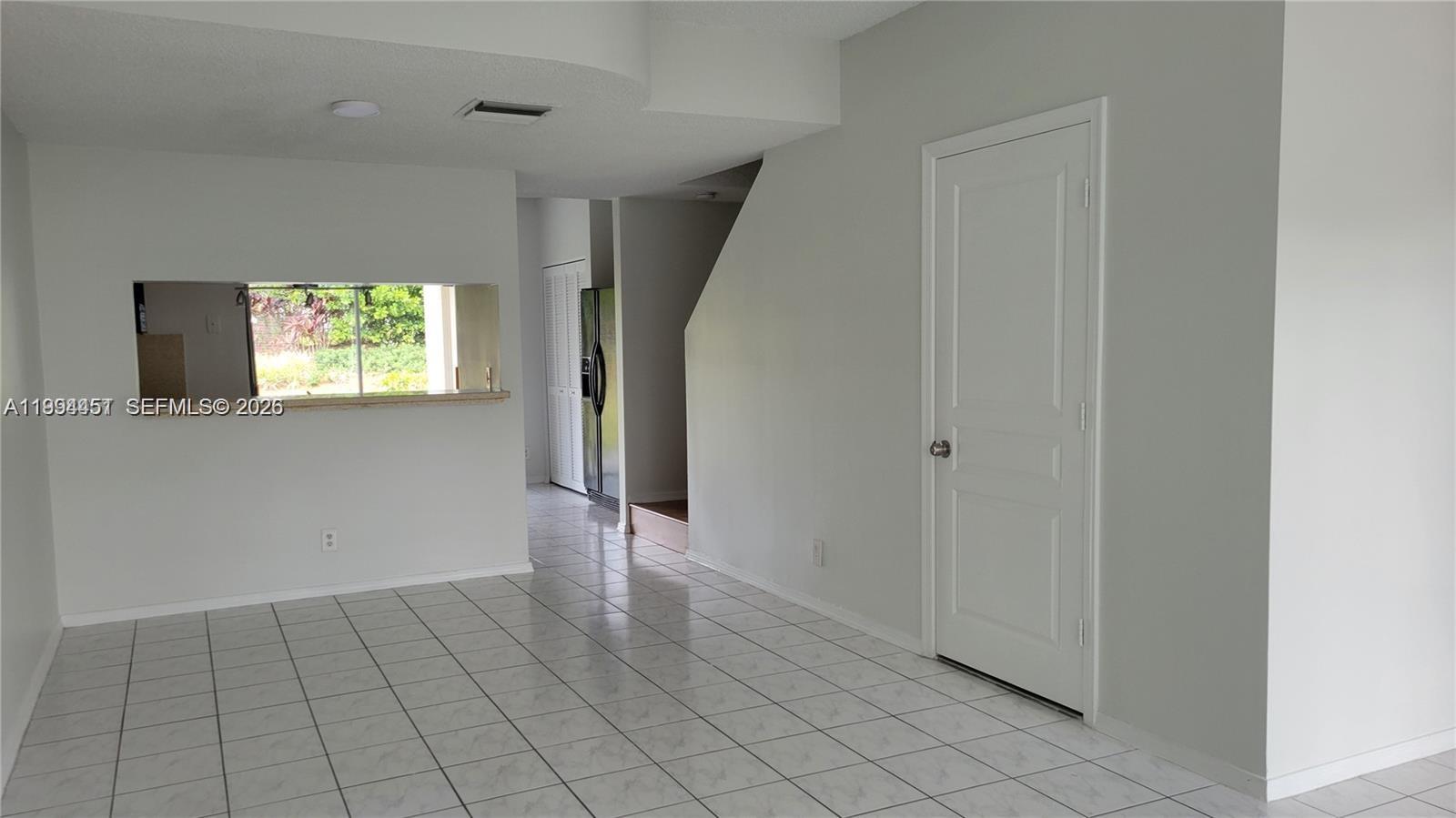 An empty living room features white tile flooring, light gray walls, and a kitchen pass-through window — 16731 Hemingway Dr, Weston FL 33326, WESTON, FL