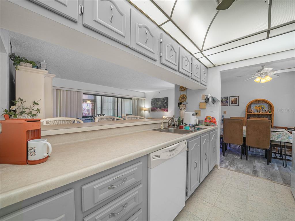 A kitchen features gray cabinets, a white dishwasher, a laminate countertop, and a pass-through window — 121 LA CASA UNIT 5, LAKE WALES, FL