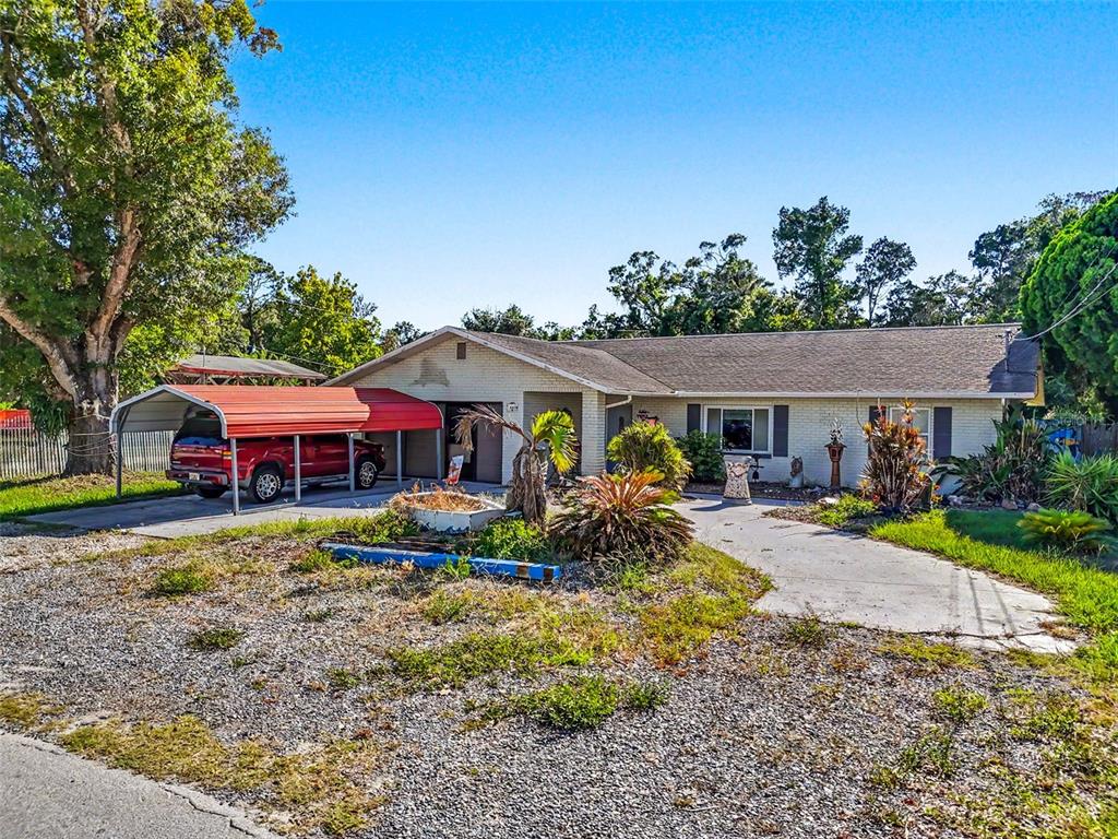 A single-story brick house with a red metal carport and a gravel front yard — 7813 LEO KIDD AVENUE, PORT RICHEY, FL