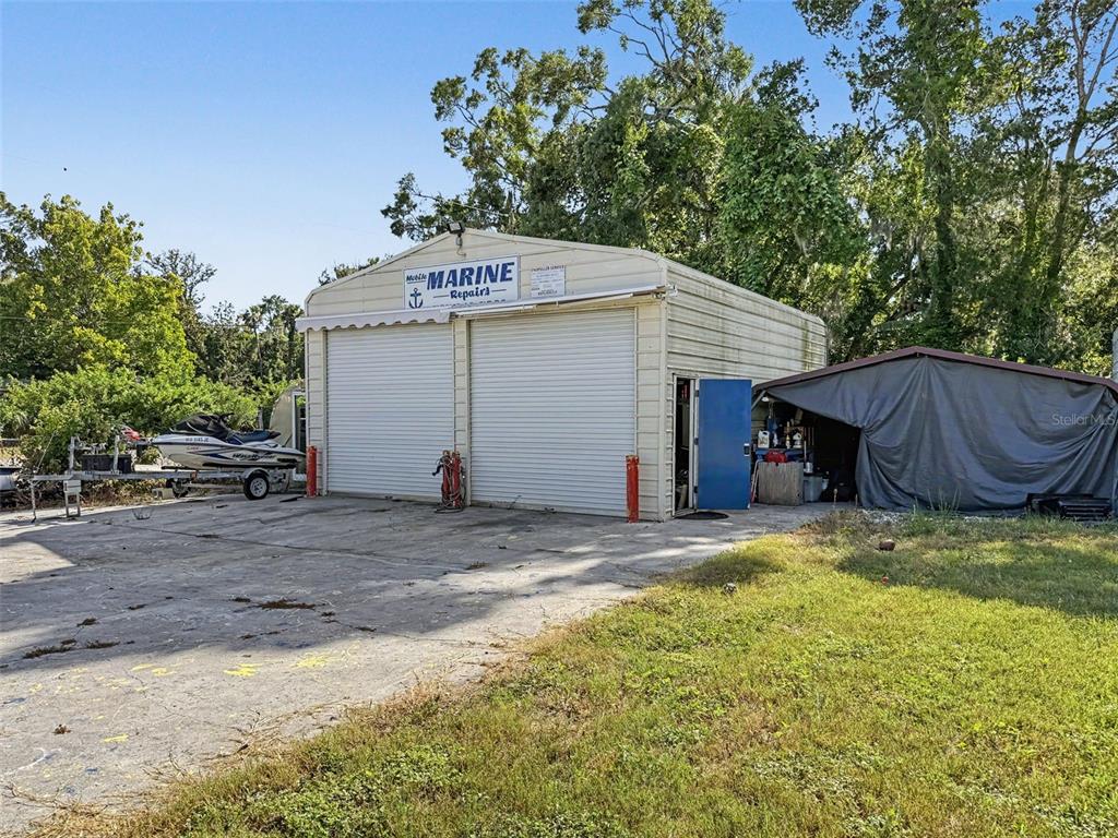 A metal workshop building with two roll-up doors and an adjacent covered storage area — 7813 LEO KIDD AVENUE, PORT RICHEY, FL