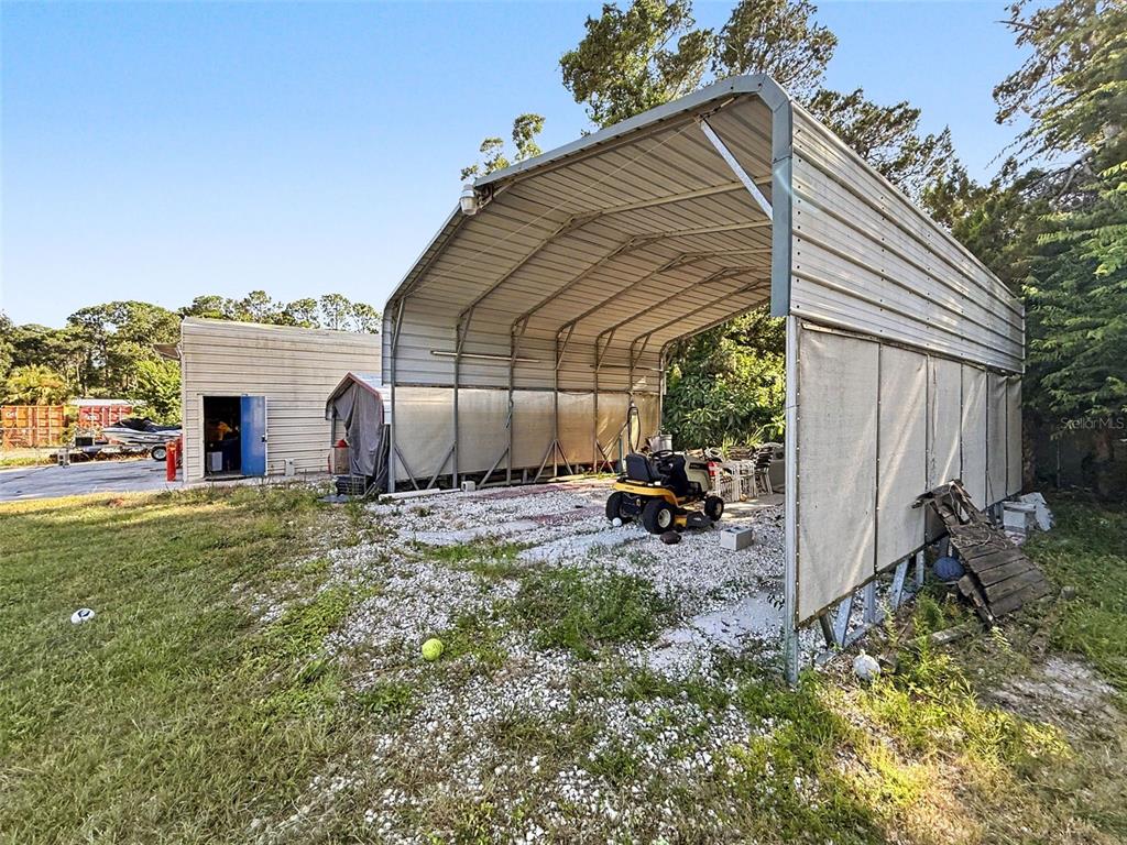 A metal carport with a gravel floor sits next to a small storage building — 7813 LEO KIDD AVENUE, PORT RICHEY, FL