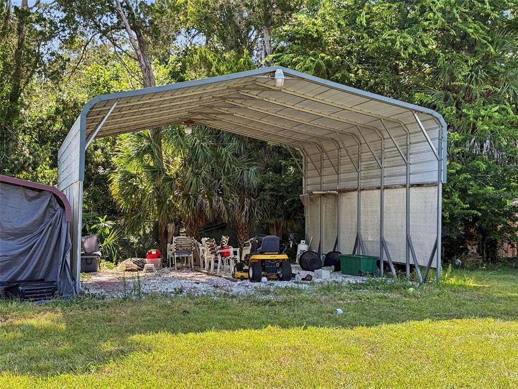 A metal carport stands over a gravel area with a lawn mower and patio chairs — 7813 LEO KIDD AVENUE, PORT RICHEY, FL