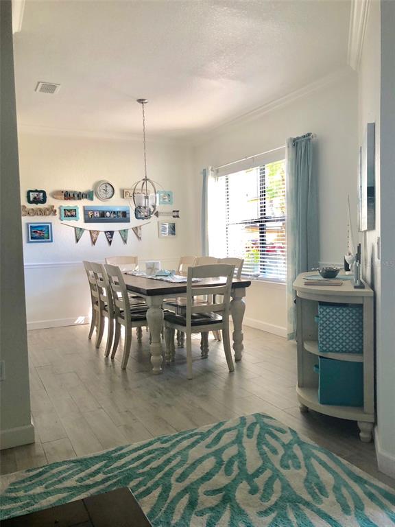 A dining room features a wooden table, six chairs, light wood flooring, and coastal decor — 2107 PORTOFINO PLACE UNIT 3011, PALM HARBOR, FL