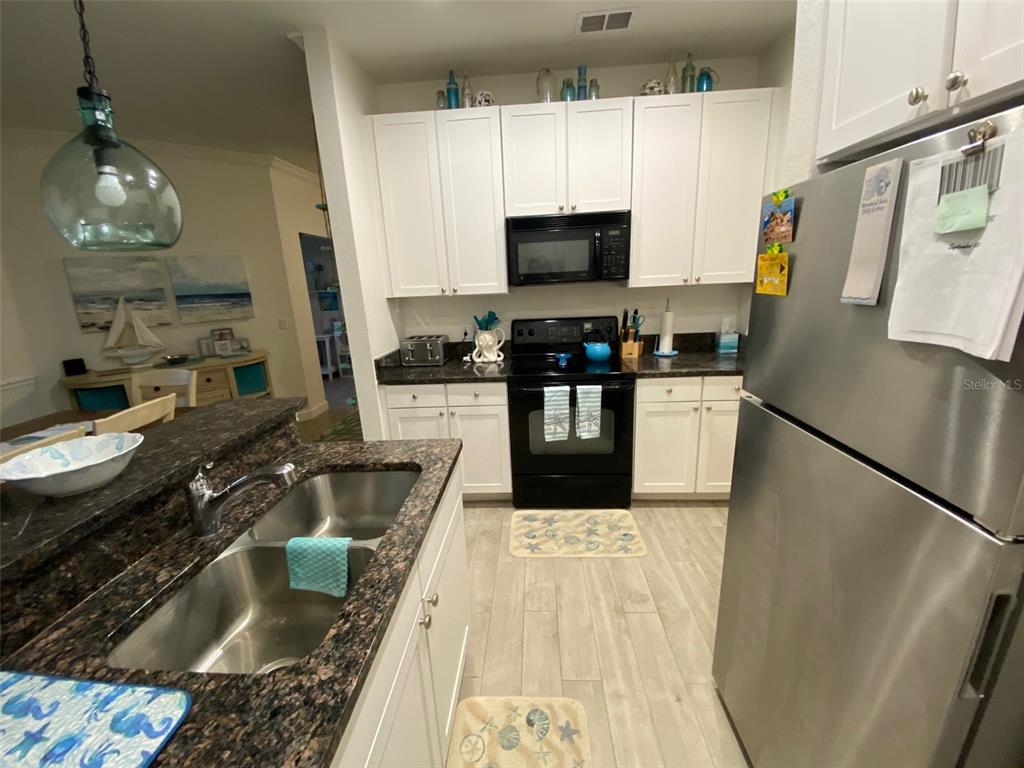 A kitchen features white cabinets, dark granite countertops, stainless steel appliances, and wood-look tile flooring — 2107 PORTOFINO PLACE UNIT 3011, PALM HARBOR, FL