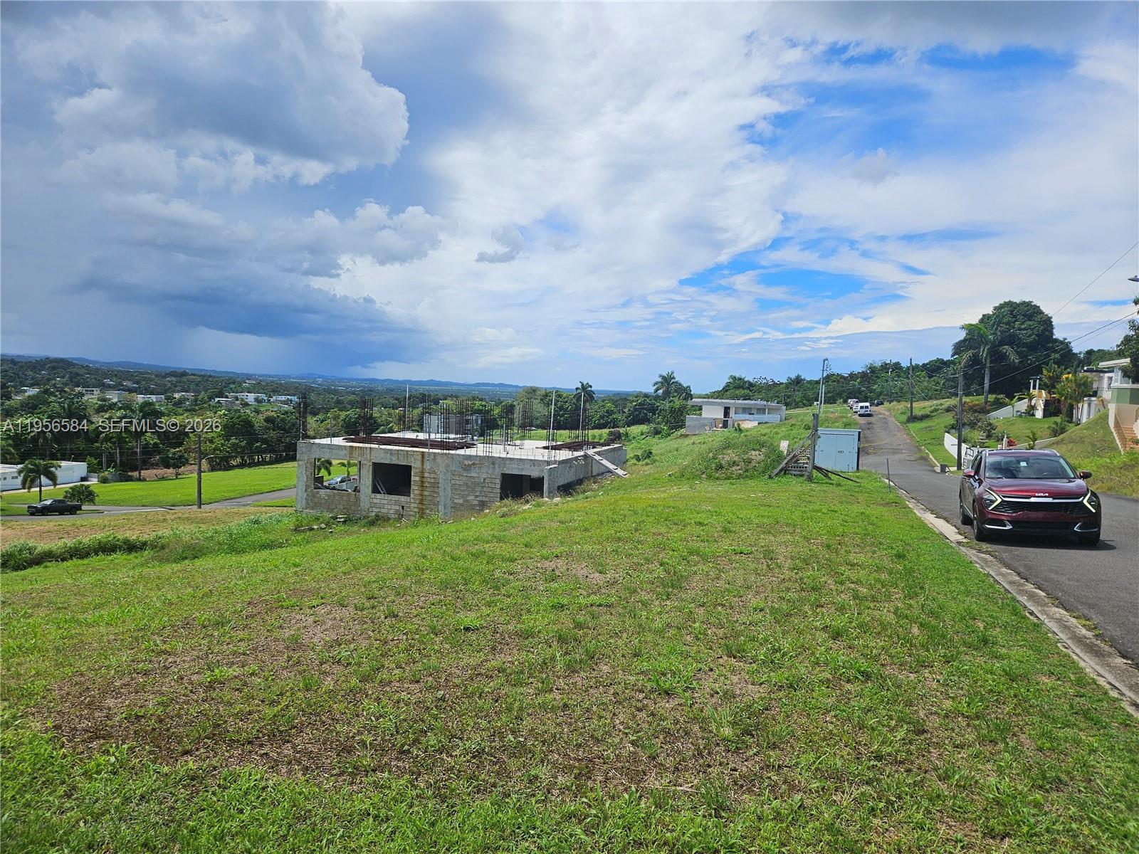 A red SUV is parked on a road next to a concrete building under construction — URB MIRADOR DE PALMER . SOLAR 41 RIO GRANDE, PR 00745, PR